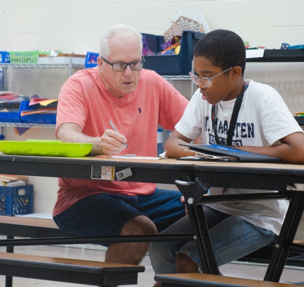 An adult mentor tutors a student who is completing his homework.